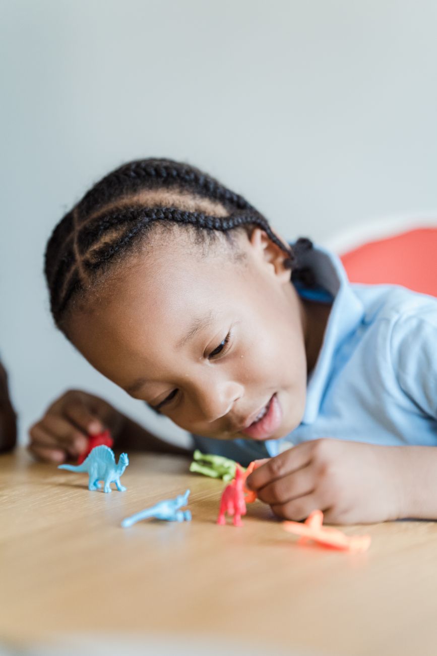 Young child playing with toy dinosaurs across a table from an adult