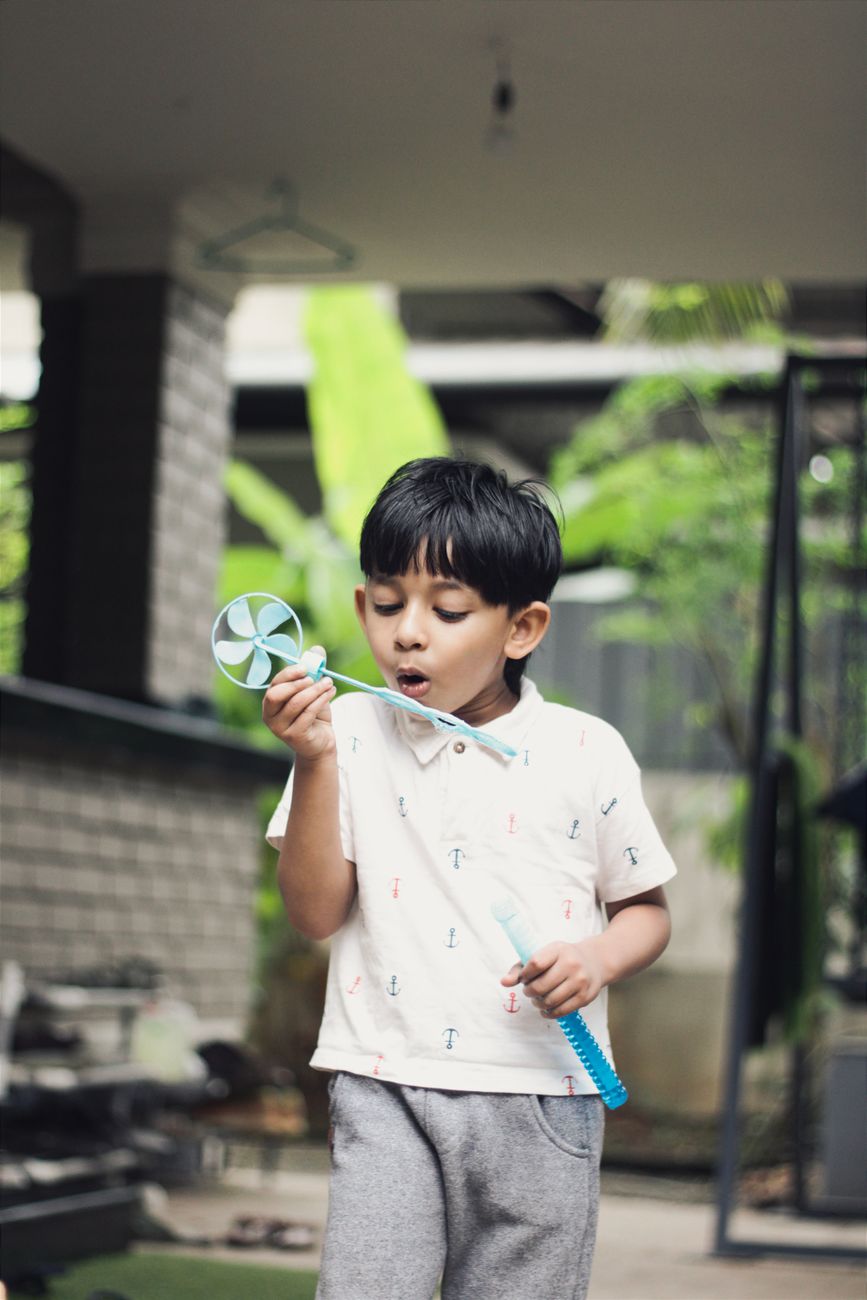 Young Indian boy blowing on a pinwheel toy, mouth forming a sound