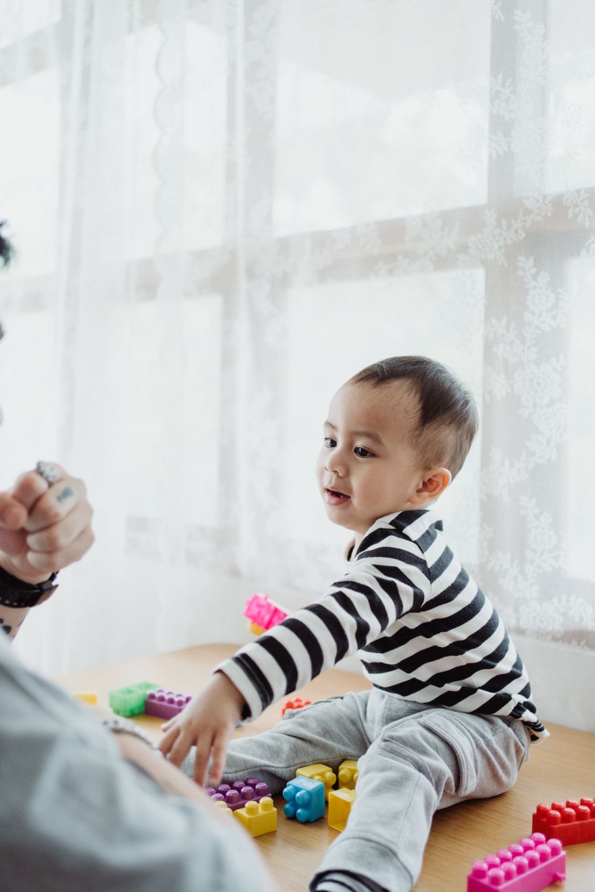 Toddler playing with colourful building blocks at a table with a parent